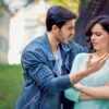Man gesturing angrily at a woman who looks upset during a confrontation in a park near a railing