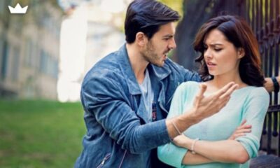 Man gesturing angrily at a woman who looks upset during a confrontation in a park near a railing