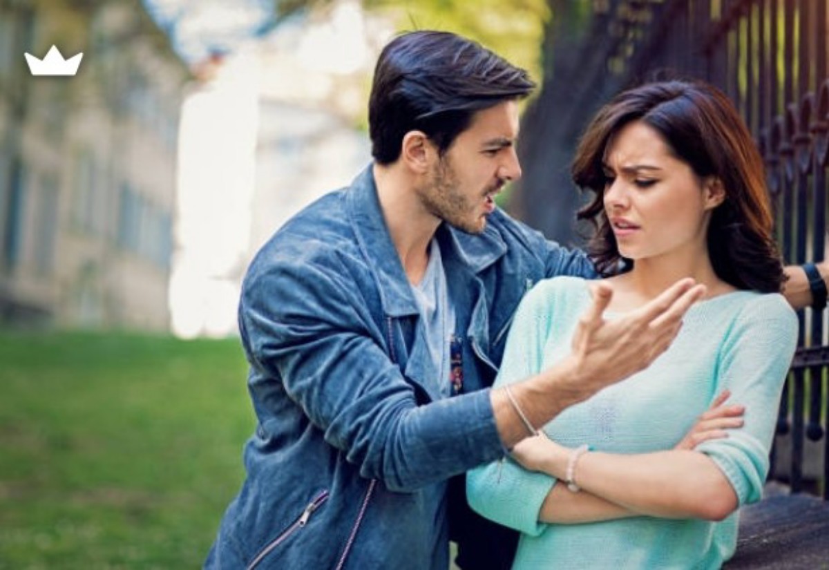 Man gesturing angrily at a woman who looks upset during a confrontation in a park near a railing