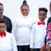 A family of five posing for a formal portrait: two adults and three children, all dressed in white shirts; two boys wear red bow ties, the girl in a white turtleneck, and the mom wears a floral dress.