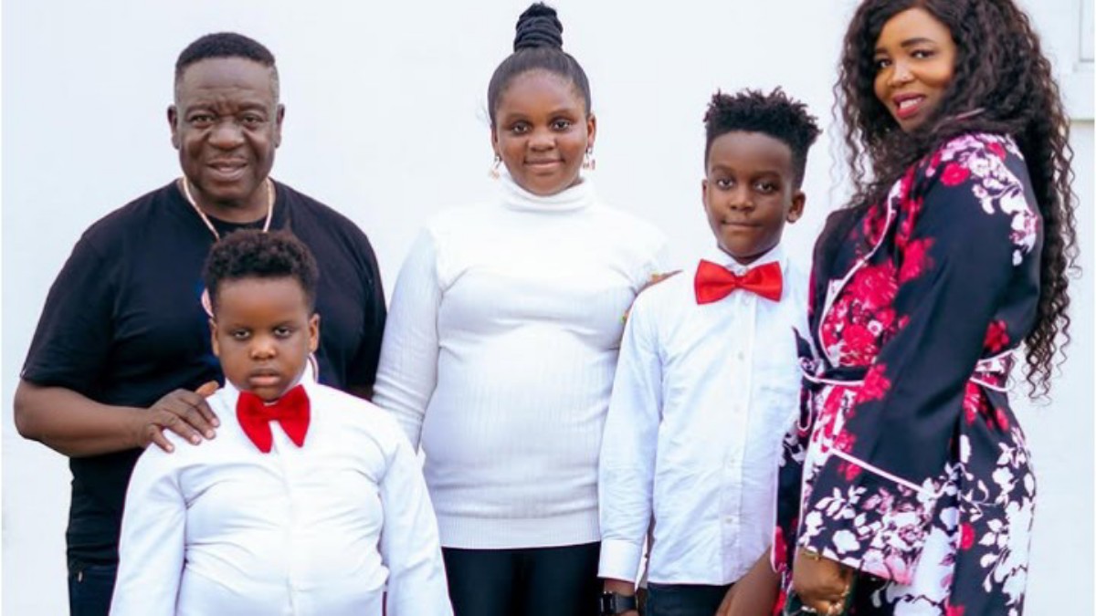 A family of five posing for a formal portrait: two adults and three children, all dressed in white shirts; two boys wear red bow ties, the girl in a white turtleneck, and the mom wears a floral dress.