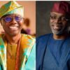 Two men smiling side by side: left in bright turquoise and gold traditional Nigerian attire with a patterned cap and bead necklace; right in blue medical scrubs with a red surgical cap.