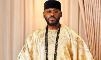 Portrait of a man in a gold traditional agbada with a black cap, glasses, and long black beads.