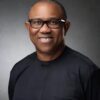 Smiling man wearing black glasses and a dark shirt in a gray studio portrait backdrop.
