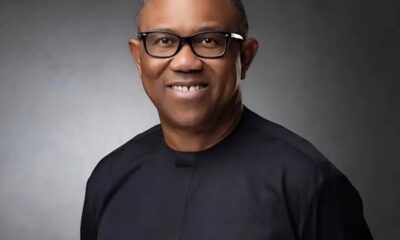 Smiling man wearing black glasses and a dark shirt in a gray studio portrait backdrop.