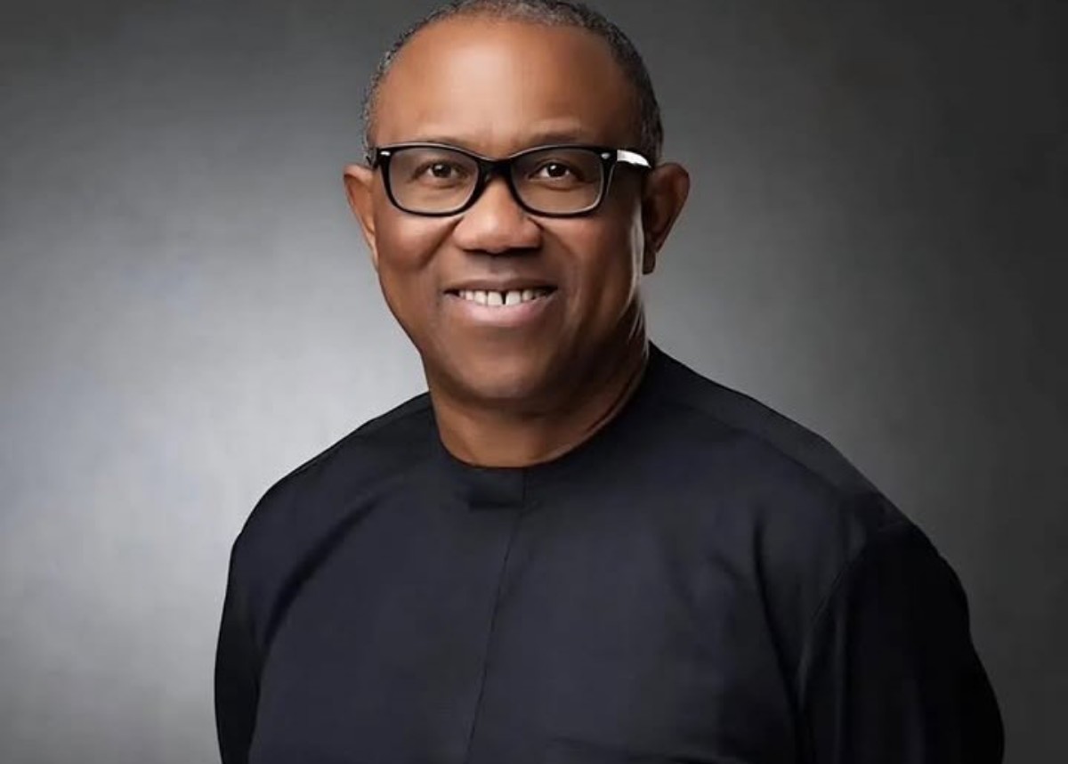 Smiling man wearing black glasses and a dark shirt in a gray studio portrait backdrop.