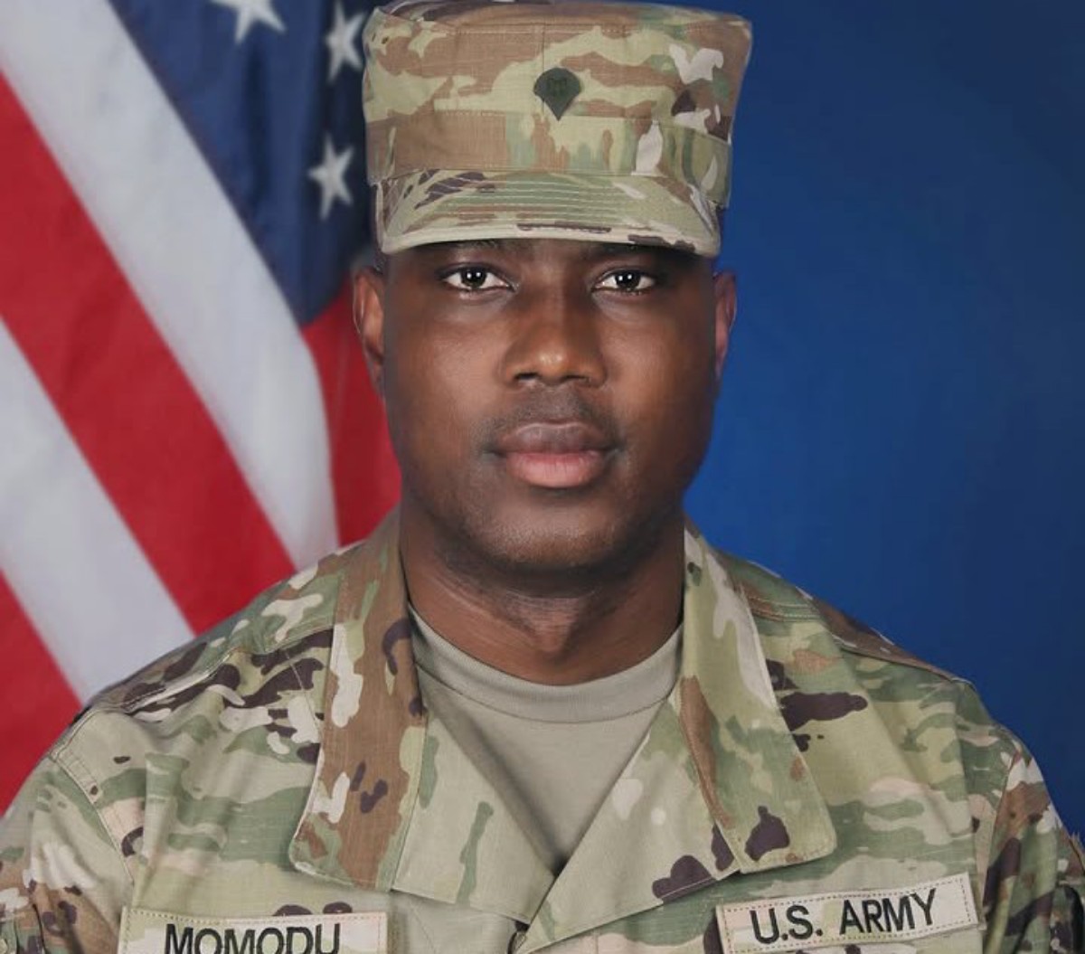 Portrait of a U.S. Army soldier in camouflage uniform with an American flag backdrop in the background.