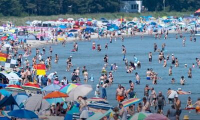 Busy beach filled with people swimming and sunbathing under colorful umbrellas and tents along the shore.