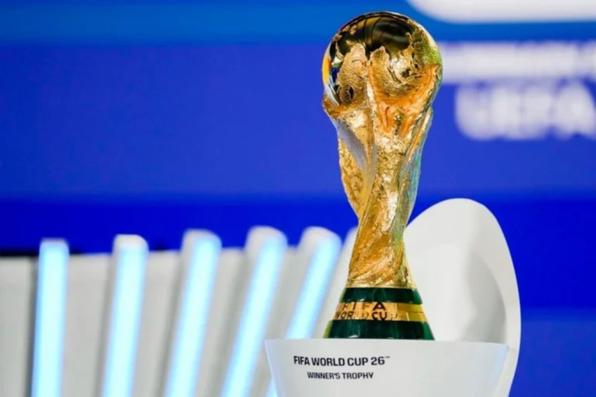 FIFA World Cup trophy close-up on a white pedestal with a blue background, shimmering gold surface visible