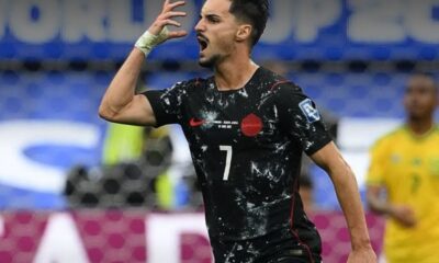 Soccer player in a black Canada jersey with number 7 celebrating on the field, mouth open in a shout.