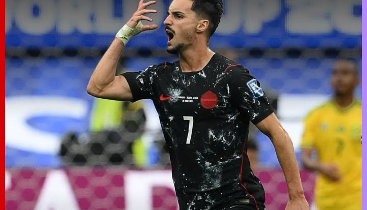 Soccer player in a black Canada jersey with number 7 celebrating on the field, mouth open in a shout.