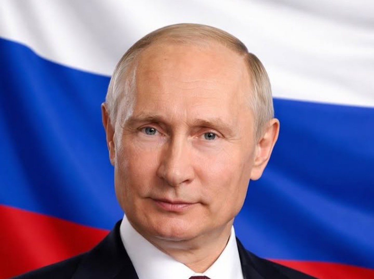 Close-up portrait of a mature man in a dark suit with a white shirt, Russia's flag in the background.