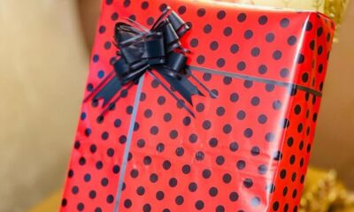 Red gift box with black polka dots, tied with a dark bow on top and a light gray ribbon crossing the front.