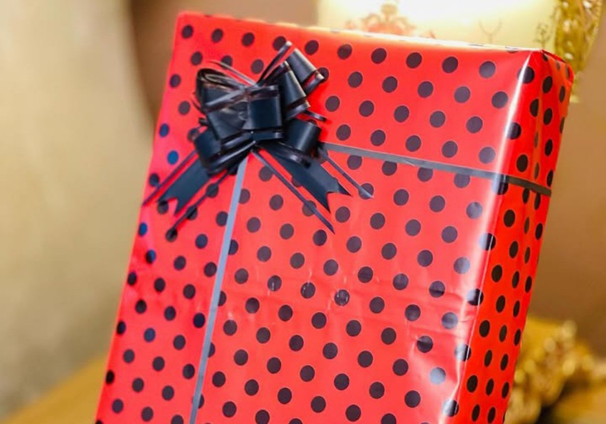 Red gift box with black polka dots, tied with a dark bow on top and a light gray ribbon crossing the front.