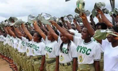 Line of Nigerian women in NYSC uniforms raising hats in a salute during a parade would be the best substitute for ALT text here, capturing the scene and purpose without unnecessary visuals.