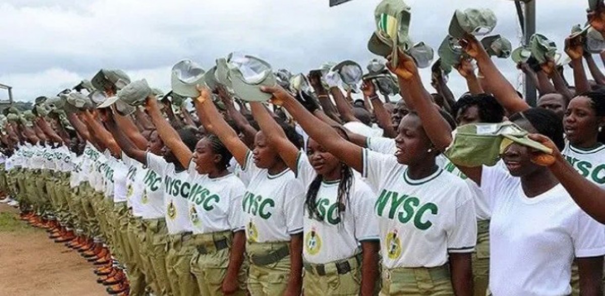 Line of Nigerian women in NYSC uniforms raising hats in a salute during a parade would be the best substitute for ALT text here, capturing the scene and purpose without unnecessary visuals.