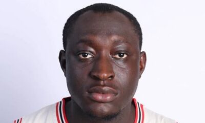 Close-up portrait of a man with a neutral expression, wearing a white jersey with red/black trim against a white background