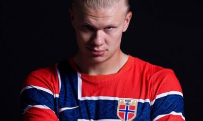 A young man with slicked-back blond hair wearing a red, white, and blue Norway football jersey with crest, posed against a dark background.