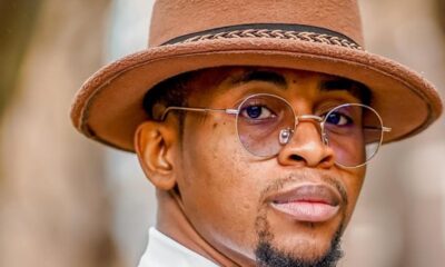 Portrait of a man wearing a brown felt hat and round sunglasses, looking over his shoulder.