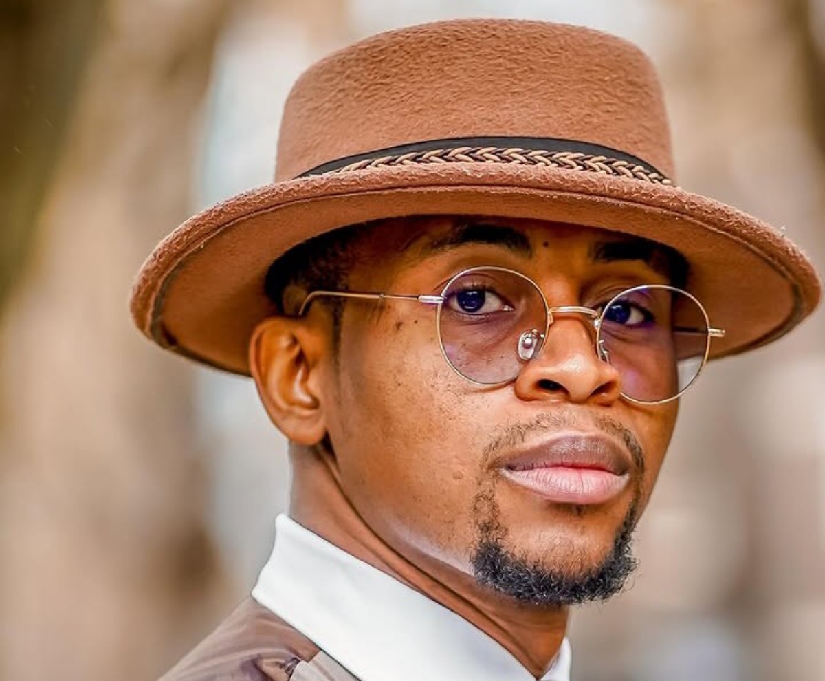 Portrait of a man wearing a brown felt hat and round sunglasses, looking over his shoulder.