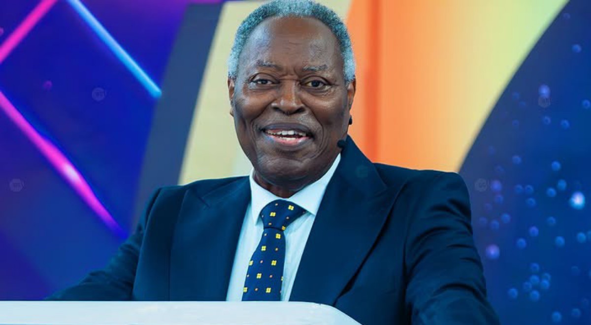 Smiling man in a navy suit delivering a speech at a podium, with a colorful abstract background behind him.
