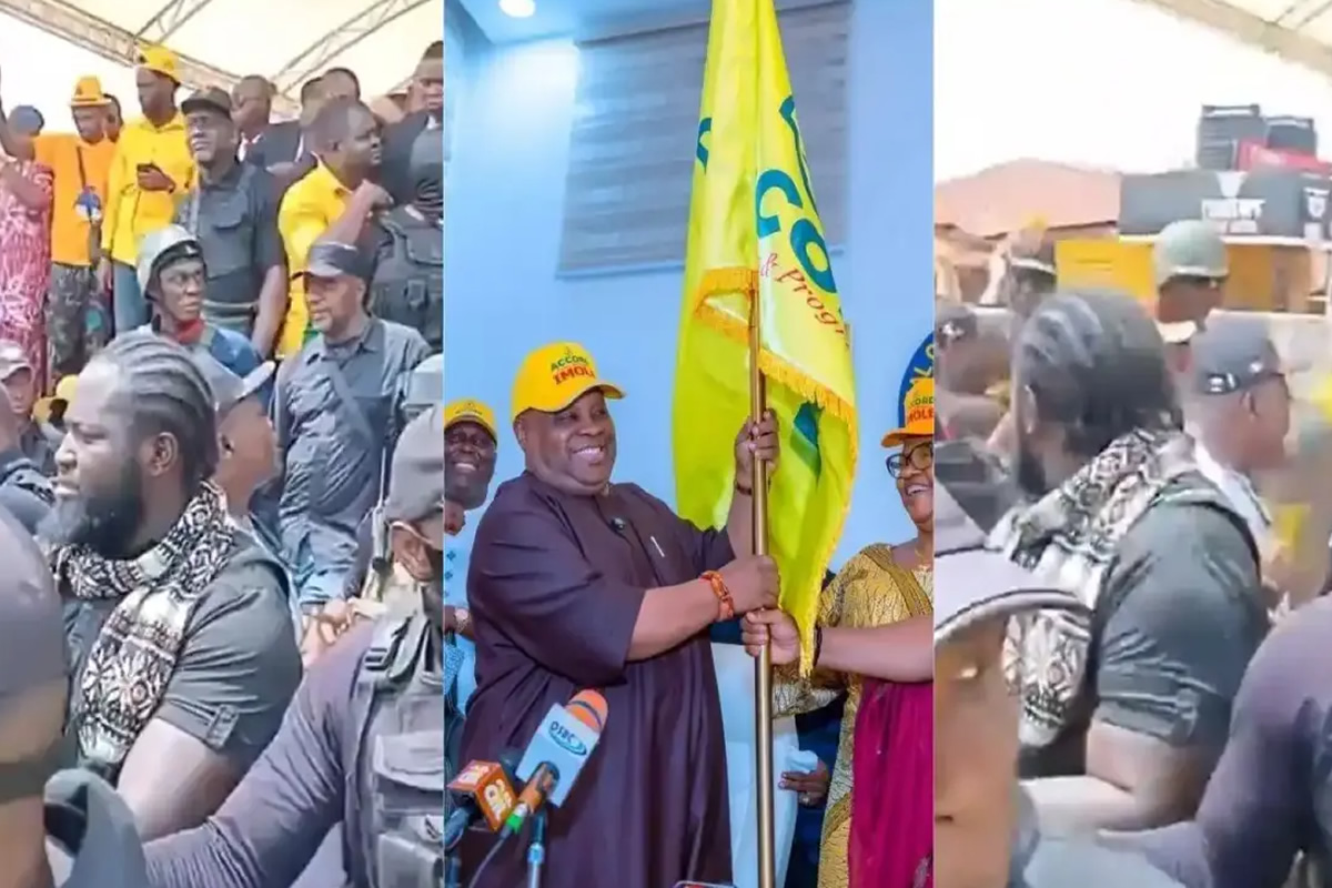 A crowd of people at a political event, with a central figure holding a yellow flag and smiling for cameras.