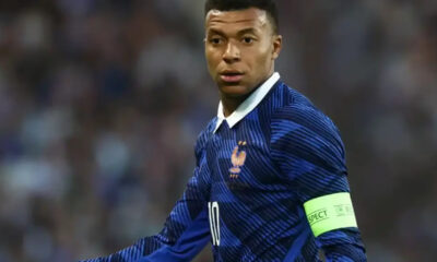 Professional soccer player in a blue France jersey with white collar, wearing a neon captain's armband during a match.
