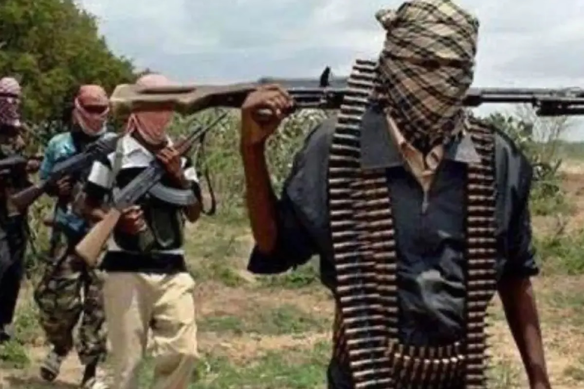 Masked group of gunmen walking through a rural field, rifles raised; front man has a scarf over his face and an ammo belt.