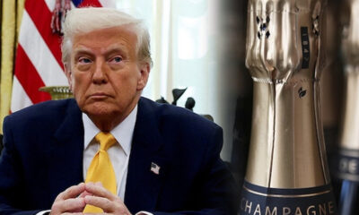 Former President Donald Trump in a navy suit and yellow tie, hands folded, with the U.S. flag in the background.