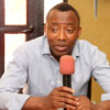 Man in a light blue shirt speaks into a pink microphone during an interview.