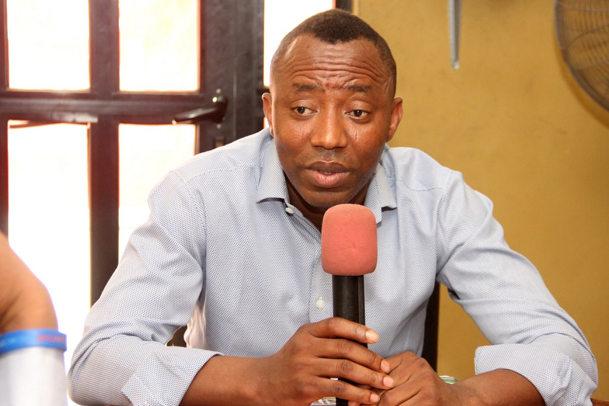 Man in a light blue shirt speaks into a pink microphone during an interview.