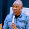 Nigeria Customs officer in uniform speaking into a handheld microphone at a formal event, seated at a table with a white chair cover behind him.