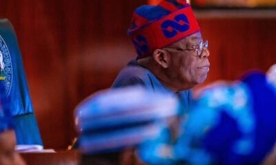 Side profile of an older man wearing a red and blue traditional cap and glasses, seated in a meeting room.