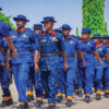 Group of uniformed cadets marching in formation, wearing blue uniforms with red collars and yellow accents outdoors.