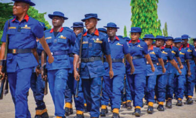 Group of uniformed cadets marching in formation, wearing blue uniforms with red collars and yellow accents outdoors.