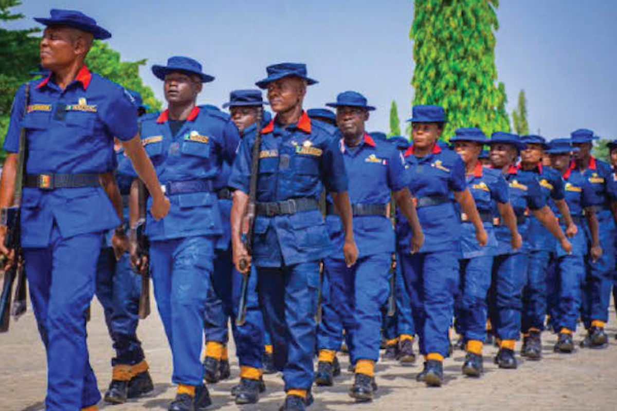 Group of uniformed cadets marching in formation, wearing blue uniforms with red collars and yellow accents outdoors.