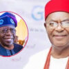 Man in white attire with red cap and beaded necklace smiles at camera; inset shows another smiling man in blue traditional hat.