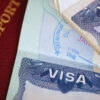 Close-up of a red passport cover beside a stack of currency notes and a Visa card partially visible (informative image: travel documents and money).