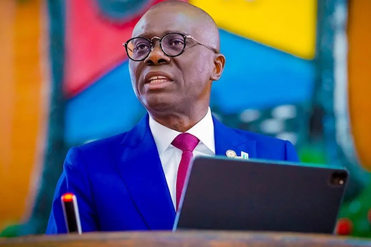 Man in a blue suit and pink tie speaks at a podium with a tablet.