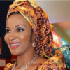 Smiling woman wearing a bright orange and purple headwrap with matching outfit and jewelry in an indoor event setting