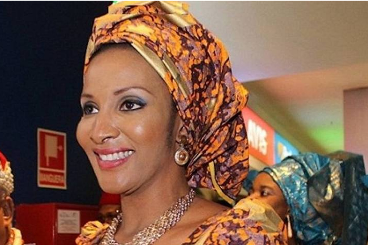 Smiling woman wearing a bright orange and purple headwrap with matching outfit and jewelry in an indoor event setting
