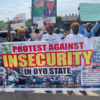Protestors hold a large banner reading 'Protest Against Insecurity in Oyo State' with people behind and signs demanding end to insecurity, outdoors