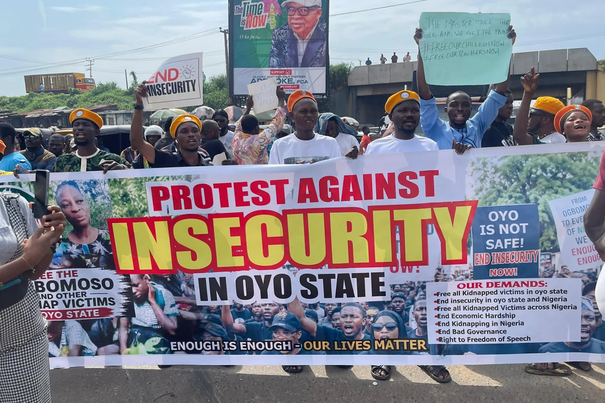 Protestors hold a large banner reading 'Protest Against Insecurity in Oyo State' with people behind and signs demanding end to insecurity, outdoors