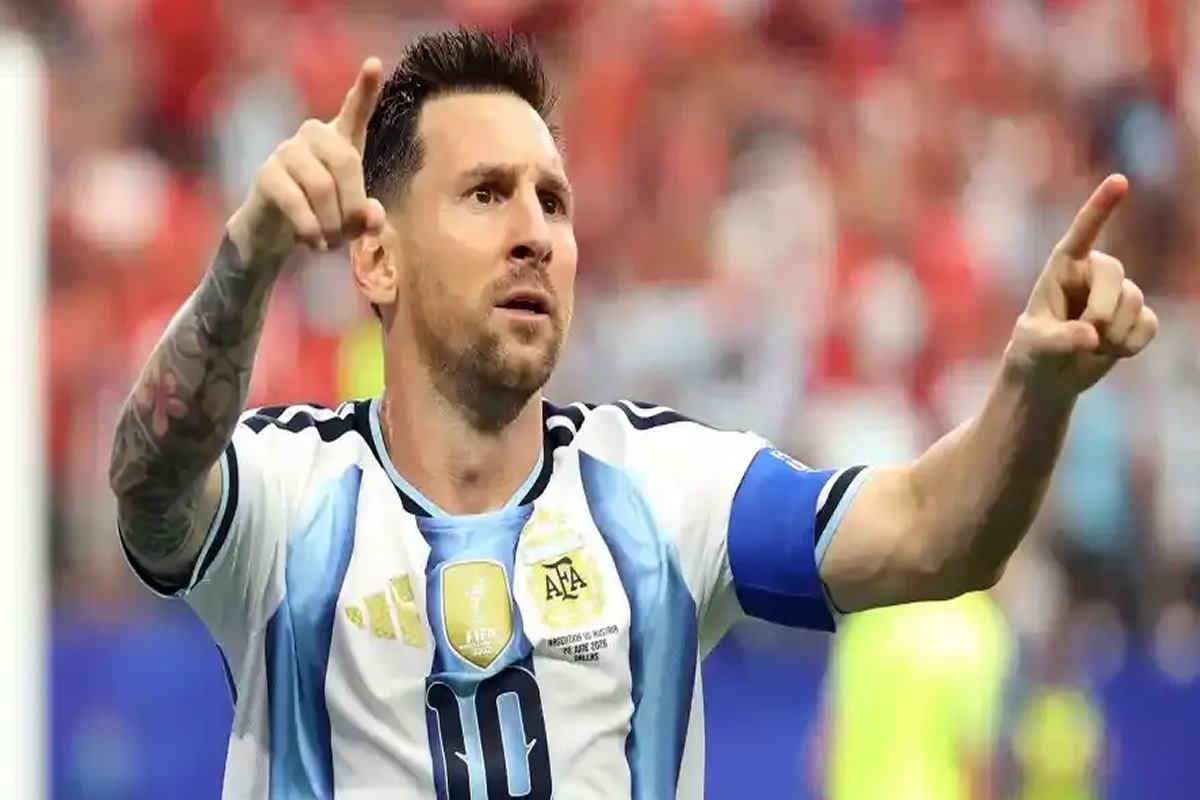 Argentinian footballer in a light blue and white jersey with a captain's armband raises both arms and points, celebrating a goal.
