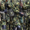 Soldiers in camouflage uniforms standing in a line, holding rifles with gear and kneepads visible.