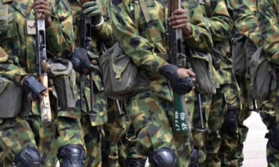 Soldiers in camouflage uniforms standing in a line, holding rifles with gear and kneepads visible.