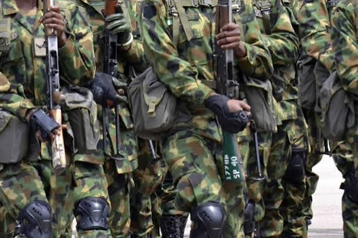 Soldiers in camouflage uniforms standing in a line, holding rifles with gear and kneepads visible.