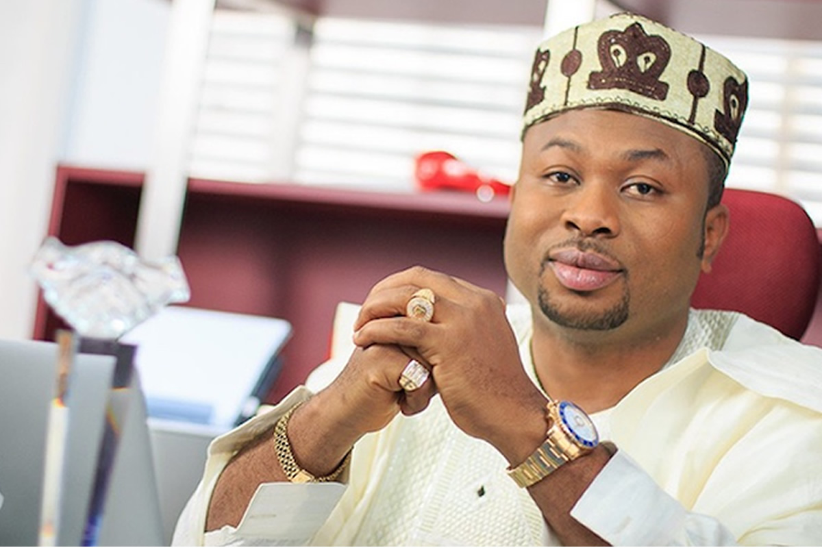 Man wearing traditional Nigerian attire and cap sits at a desk with hands clasped