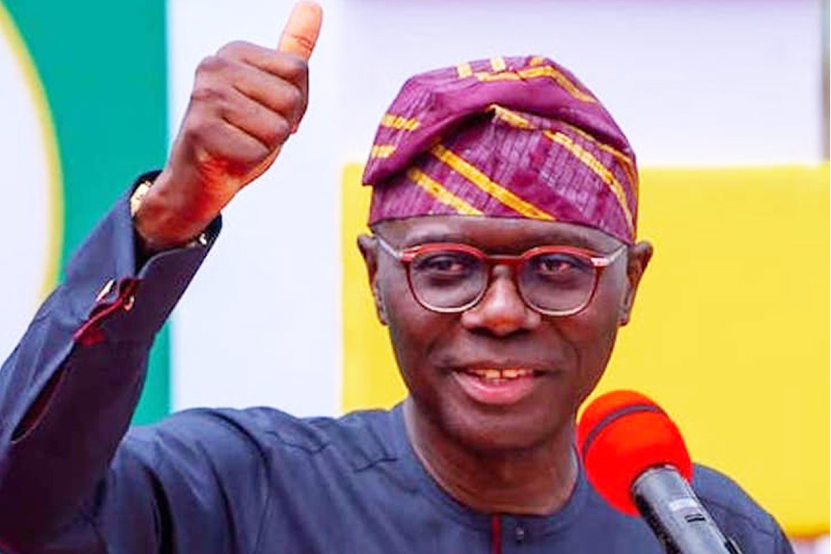 Smiling man in glasses and a purple patterned cap gives a thumbs up beside a red microphone during a speech.
