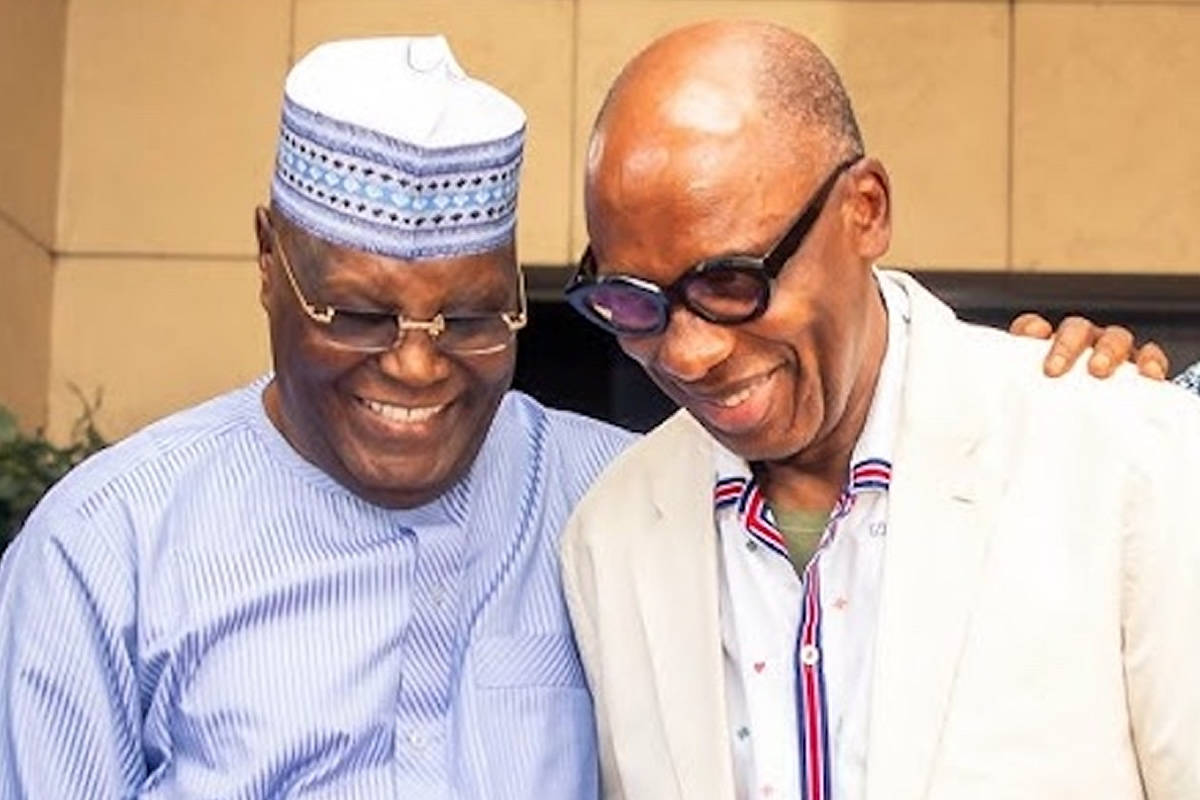 Two friends smiling and posing together, one wearing a patterned hat and striped shirt, the other in a light blazer and glasses.